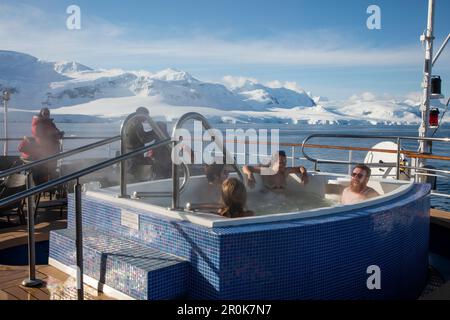 I passeggeri si rilassano in una vasca idromassaggio a bordo di una nave da crociera da spedizione MV Sea Spirit (spedizione Poseidon) con vista sulle montagne innevate dello stretto di Gerlache, Foto Stock