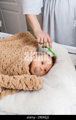 Spazzola a mano della madre i primi capelli del neonato, il bambino è adagiato in una culla coperta morbida e intima e succhiata, succhietto, piumino Foto Stock