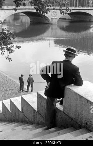 Herr betrachtet zwei Angler am Rand der Seine, der Pont Saint Michel im Hintergrund, Parigi 1940. Gentleman guardando due pescatori sul bordo della Senna, il Pont Saint Michel sullo sfondo, Parigi 1940. Foto Stock