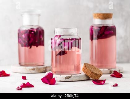Acqua dolce fatta in casa di rosa o sciroppo in bottiglie di vetro con petali rosa in esso. Concetto di sano cibo estivo. Messa a fuoco selettiva. Spazio di copia. Foto Stock