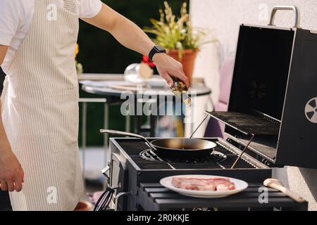 Uomo che prepara il cibo all'aperto su barbecue grill. Aggiungere olio d'oliva sulla padella per preparare la bistecca con osso a T. Foto Stock