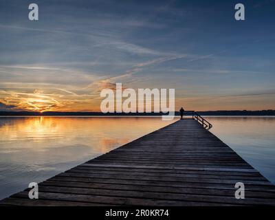 Una donna in piedi su un molo al tramonto sulla riva orientale del lago Starnberg, Ambach, alta Baviera, Germania Foto Stock