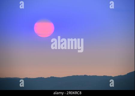 Sunset over the Mountains. The orange sun dips below the horizon. A breathtaking view of nature. Foto Stock