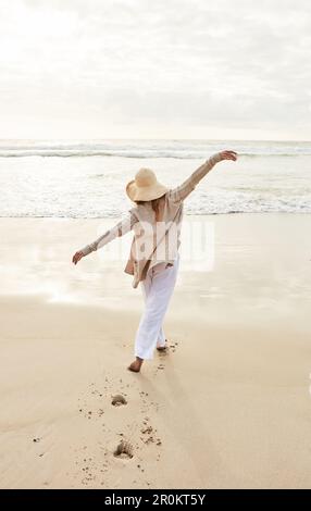 Il mare ha i suoi poteri di ringiovanimento. Ripresa da dietro di una giovane donna in piedi con le braccia distese in spiaggia. Foto Stock