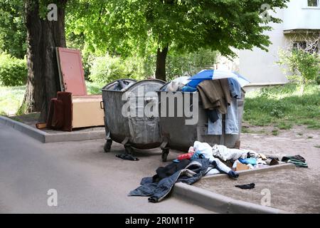 Vecchi contenitori di metallo e spazzatura sparsa sulla strada cittadina Foto Stock