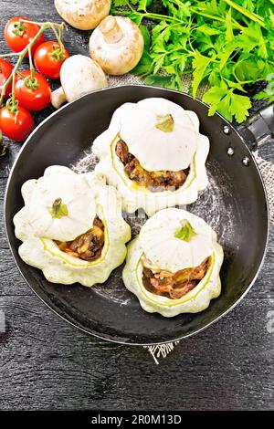 Zucca farcita con fegato, cipolle, funghi, pomodori e formaggio in una padella su un tovagliolo di tela di tela sullo sfondo di legno dall'alto Foto Stock