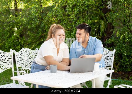 Giovane coppia asiatica chubby utilizzando un computer portatile nel parco verde all'aperto insieme. Felice uomo sorridente e donna che lavorano a distanza e avviare il proprio business insieme Foto Stock
