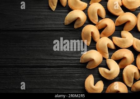 Biscotti gustosi della fortuna con predizioni su tavolo di legno nero, piatto. Spazio per il testo Foto Stock