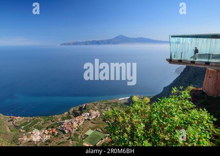 Persona in piedi in vetro Skywalk con vista sul villaggio di Agulo e tenero con Teide, patrimonio dell'umanità dell'UNESCO Teide, da Mirador de Abrante, la Gome Foto Stock