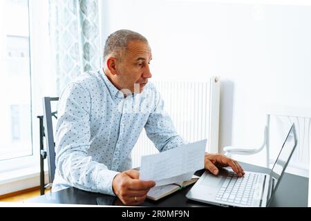 l'uomo fa i calcoli, guarda attraverso il rapporto finanziario del registratore di cassa domestico Foto Stock