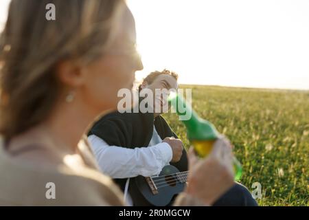 Ora legale. Bella giovane coppia godendo del tempo in campo intorno all'erba. Stile di vita, amore, datazione, concetto di vacanza. Privato. Donna che beve birra, uomo Foto Stock