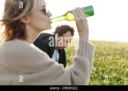 Ora legale. Bella giovane coppia godendo del tempo in campo intorno all'erba. Stile di vita, amore, datazione, concetto di vacanza. Privato. Donna che beve birra, uomo Foto Stock