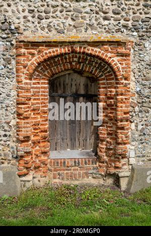 Porta Sud in mattoni rossi posta in una parete di selce vestita da fielwork presso la Chiesa di San Pietro a Weston, Suffolk Foto Stock