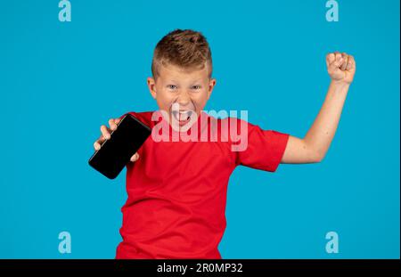 Smartphone Little Boy Holding overjoyed con schermo vuoto e festeggiamento del successo Foto Stock