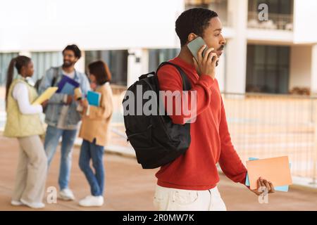 Serio occupato afro-americano studente in casual con le chiamate dello zaino per telefono, pronto per lo studio Foto Stock