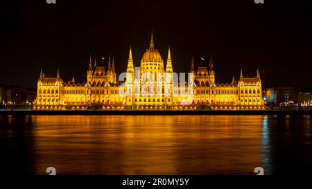 Il Parlamento di Budapest illuminato di notte con il Danubio in primo piano Foto Stock