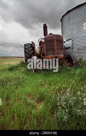 Basso angolo di macchina agricola arrugginita con ruote enormi parcheggiate su prato verde vicino fienile in campagna Foto Stock