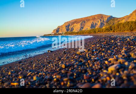 Ciottoli neri alla spiaggia di Avis e Mesa Vouno. Si trova vicino all'estremità meridionale dell'aeroporto internazionale di Santorini. Kamari Grecia,2013 Foto Stock