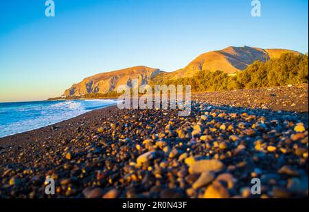 Ciottoli neri alla spiaggia di Avis e Mesa Vouno. Si trova vicino all'estremità meridionale dell'aeroporto internazionale di Santorini. Kamari Grecia,2013 Foto Stock