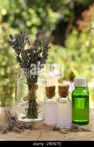 Bellissimi fiori di lavanda e bottiglie di olio essenziale su ceppo di legno Foto Stock