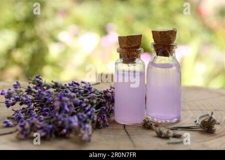 Bella lavanda fiori e bottiglie di olio essenziale su ceppo di legno, primo piano Foto Stock