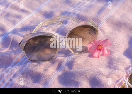 Bellissimi occhiali da sole con fiori tropicali su coperta rosa, primo piano Foto Stock