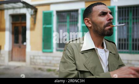 Un serio uomo arabo accende una sigaretta mentre si trova fuori con emozione penosa Foto Stock