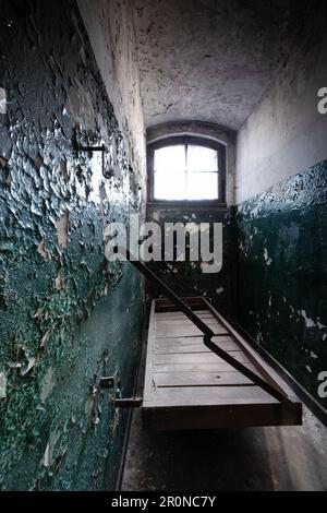 Vecchia cella di prigione con piattaforma di legno originale e vernice di peeling sulle pareti, ex prigione di corte distrettuale a Berlino Köpenick, Germania Foto Stock