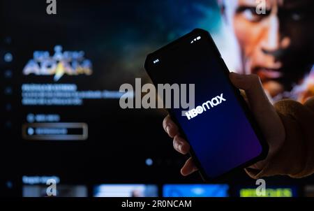 Una persona che tiene un telefono cellulare davanti allo schermo di un computer con il logo HBO Max Foto Stock