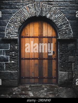 Una vibrante porta ad arco del castello in legno arancione restaurata circondata da decorazioni in pietra e da un rustico muro di pietra intatto Foto Stock