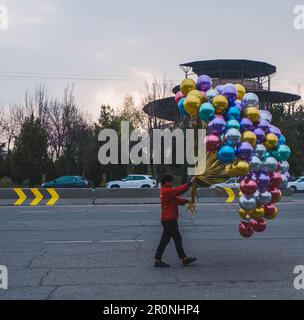 Un giovane uomo che cammina lungo la strada tenendo un mazzo di palloncini multicolore. Tashkent, Uzbekistan. Foto Stock