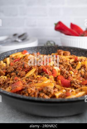 Maccheroni con carne macinata, pomodori, cipolle, peperoni, aglio ed erbe in padella. Piatto facile da pan Foto Stock