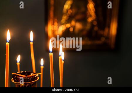 candele funerarie bruciano sull'altare con icona sfocata sullo sfondo in chiesa scura Foto Stock