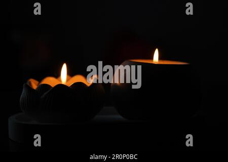 Un set di candele bianche accese sfarfallano al buio su uno sfondo nero con una candela a fuoco in primo piano. Accendere una candela. Una candela che brucia Foto Stock