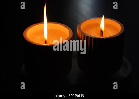 Un set di candele bianche accese sfarfallano al buio su uno sfondo nero con una candela a fuoco in primo piano. Accendere una candela. Una candela che brucia Foto Stock