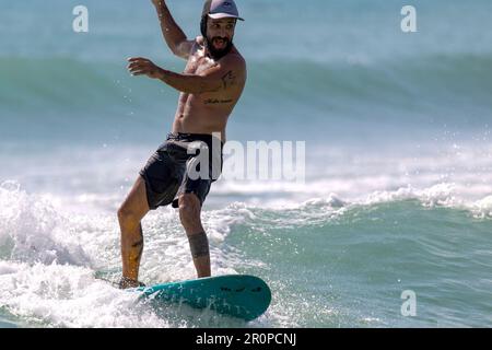 Playa del Carmen, Messico; 9 maggio 2023: Uomo sportivo che gode e mantiene l'equilibrio della sua tavola nelle calde onde del Mar dei Caraibi. Foto Stock