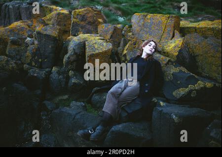 Una giovane donna con capelli ricci sdraiati sulle rocce Foto Stock