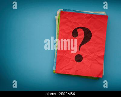 Una pila di note colorate di carta con un punto interrogativo su sfondo blu. Primo piano. Foto Stock