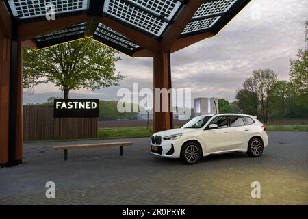 Roosendaal, Paesi Bassi - Maggio 6 2023: Stazione di ricarica rapida pubblica Fastned che carica una BMW Ix1 sull'autostrada A58 vicino alla città di Roosendaal. Foto Stock