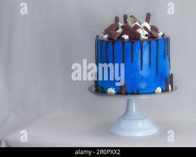 macro torta glassata blu primo piano con glassa al cioccolato fondente e dolci misti come guarnizione isolata su sfondo bianco per festeggiare Foto Stock