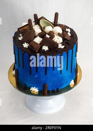 macro torta glassata blu primo piano con glassa al cioccolato fondente e dolci misti come guarnizione isolata su sfondo bianco per festeggiare Foto Stock