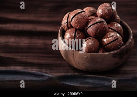 Ciotola con noci di Macadamia su tavola di legno d'epoca Foto Stock