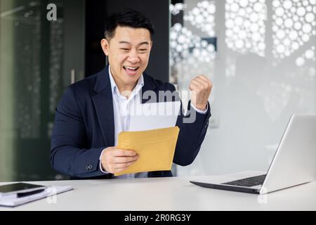 Investitore di successo imprenditore ha ricevuto una lettera di notifica dalla banca con buone notizie, l'imprenditore apre la busta legge e si rallegra della notizia, l'uomo è soddisfatto dei risultati. Foto Stock