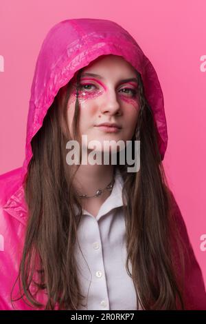 Ritratto informale giovane donna adulta con make-up palcoscenico rosa dipinto sul viso, guardando la fotocamera. Donna vestita in giacca rosa con cappuccio Foto Stock