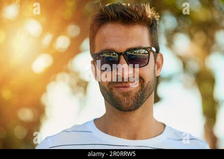 Mantenere il suo sguardo fresco per quei giorni caldi. Ritratto di un bel giovane uomo che indossa occhiali da sole in una giornata estiva all'aperto. Foto Stock