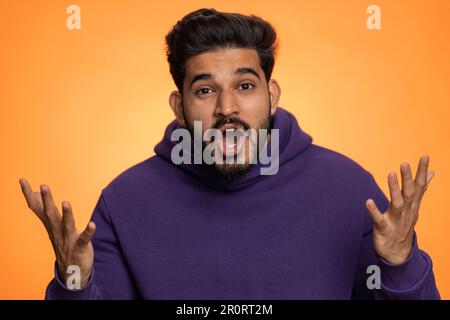 OH mio Dio, Wow. Eccitato stupito vincitore uomo alzando le mani in sorpresa guardando la telecamera con gli occhi grandi, scioccato da improvvisa vittoria. Sincero bel ragazzo indiano isolato da solo su sfondo arancione studio Foto Stock