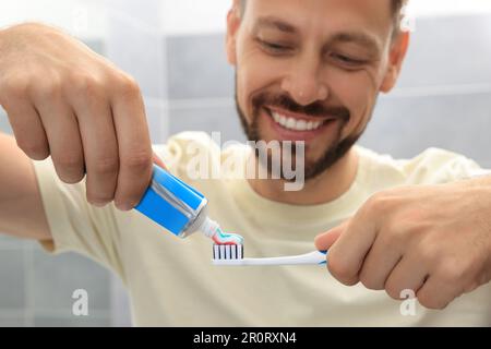 Uomo che applica dentifricio sulla spazzola in bagno, fuoco sulle mani Foto Stock