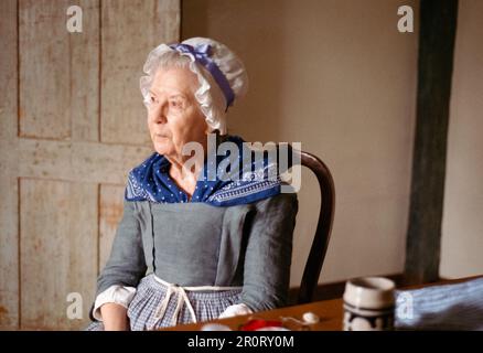 Concord, Massachusetts USA - Aprile 2023 - Una donna vestita con abiti del periodo coloniale con un cappello bianco in pizzo descrive gli eventi storici che si verificano Foto Stock