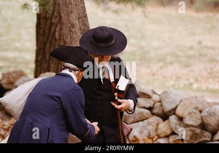 Lexington, Massachusetts USA - Aprile 2023 - Un uomo in garbo coloniale si ferma per chiacchierare con un attore vestito da predicatore che porta una Bibbia su Battle Road Foto Stock