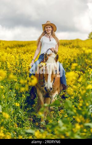 Una giovane donna bionda e il suo cavallo haflinger che si divertono in primavera all'aperto. Scena di amicizia tra una donna equestre e il suo pony Foto Stock